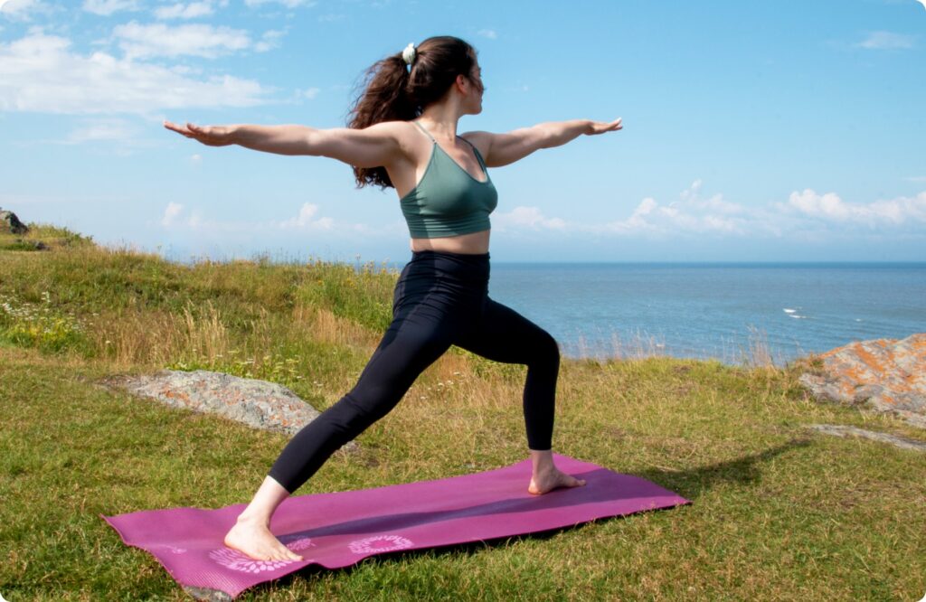 Women doing warrior B yoga pose next to the water